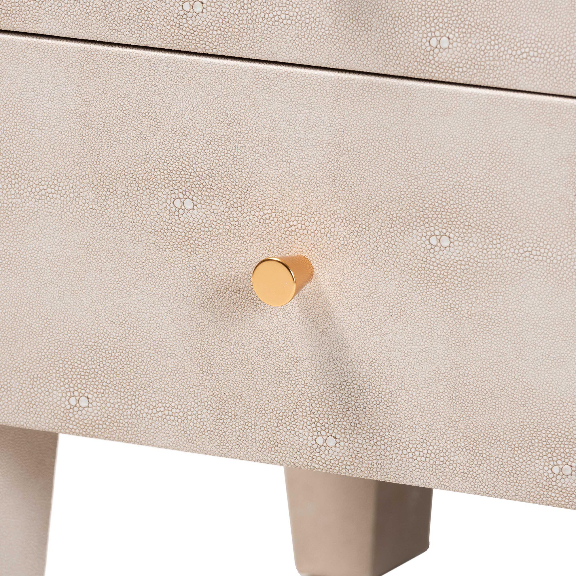 Close-up of the small gold knob on the drawer with a tiny decorative pattern on the cabinet surface.